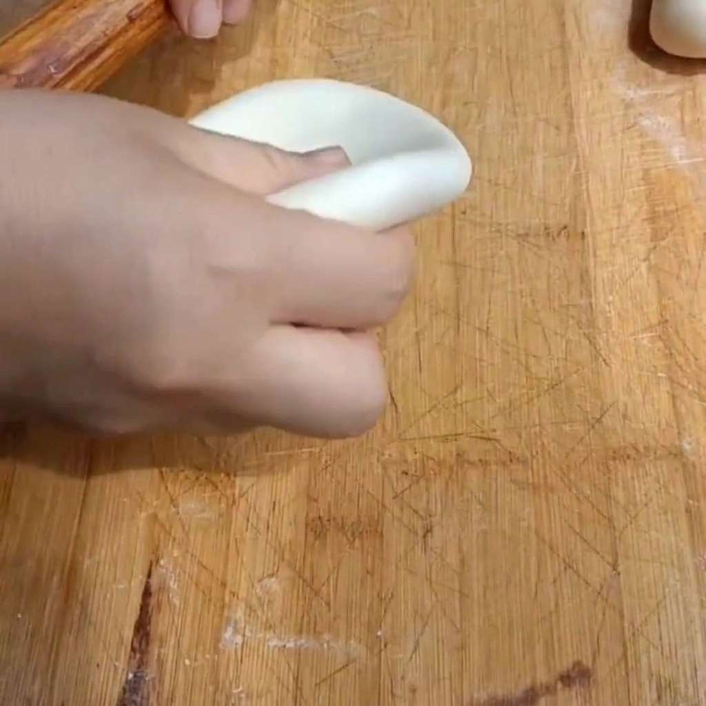 Une main utilisant un rouleau à pâtisserie en bois pour aplatir un morceau de pâte en un disque épais sur une planche en bois.