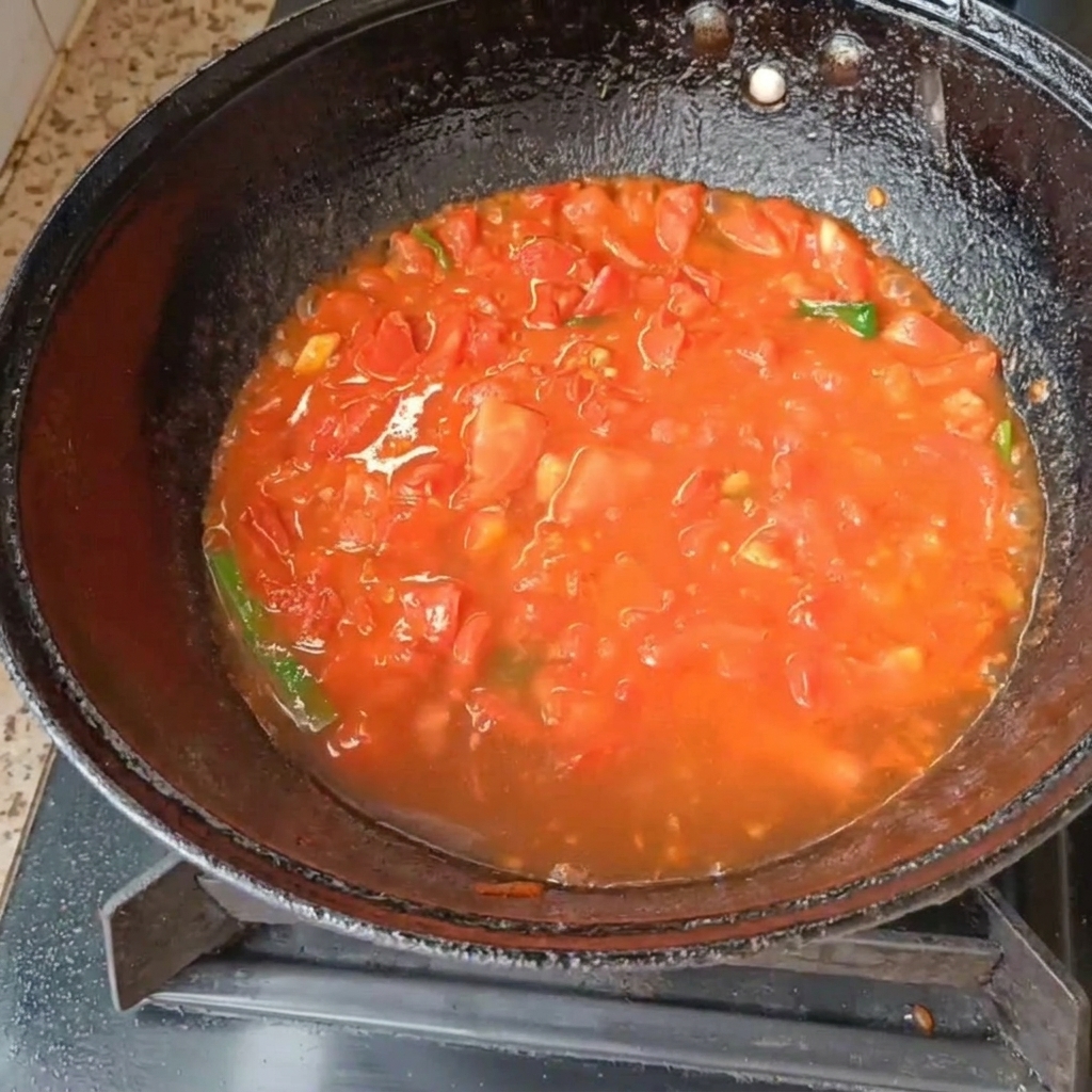 Tomates en dés et oignons verts mijotant dans leau à lintérieur dun wok noir sur une cuisinière à gaz.