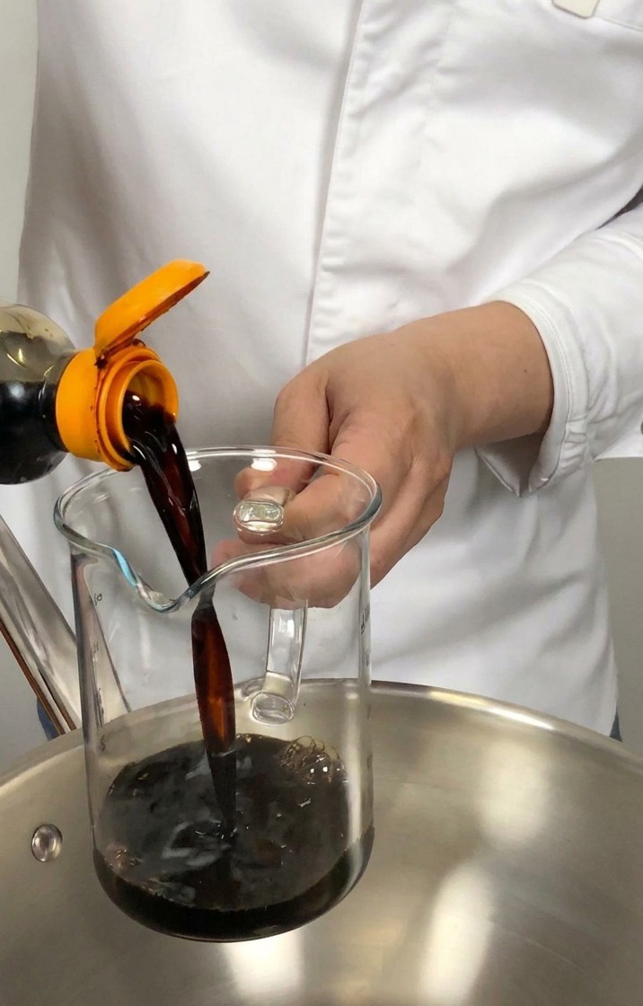 Sauce soja japonaise versée dune bouteille dans un verre doseur au-dessus dune casserole en inox.