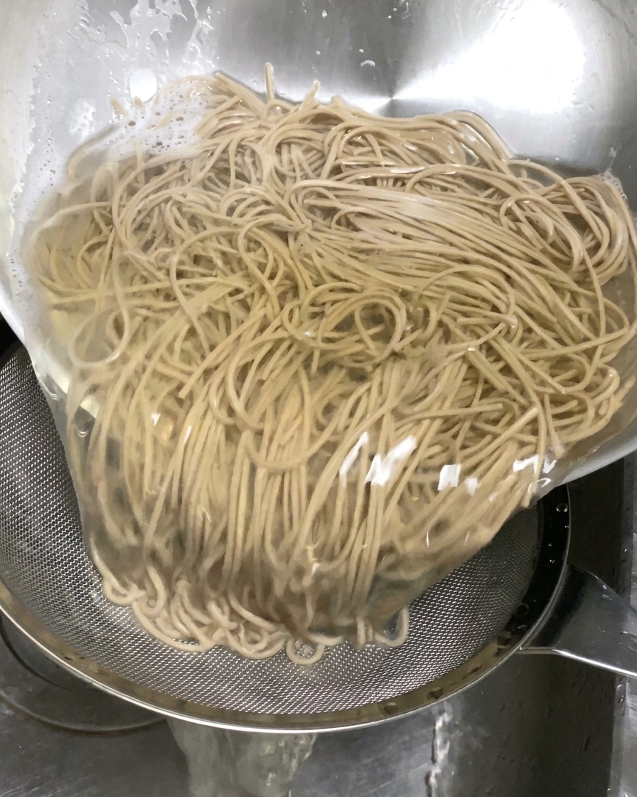 Nouilles soba cuites versées dans une passoire dans lévier pour être égouttées.