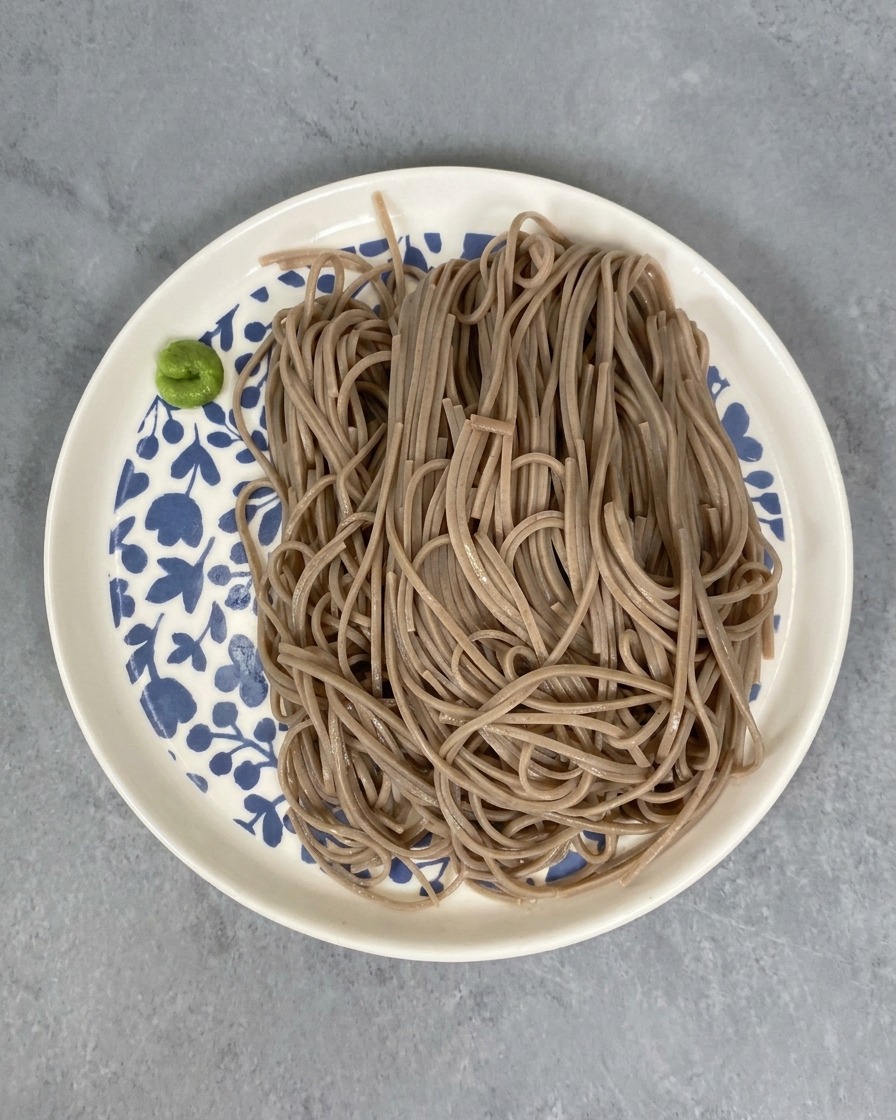 Portion de nouilles soba sur une assiette décorée avec une petite pointe de wasabi vert sur le côté.