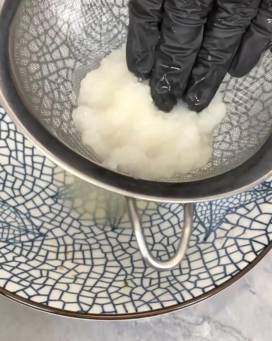 Main pressant doucement le radis râpé dans une passoire pour en extraire le jus superflu.