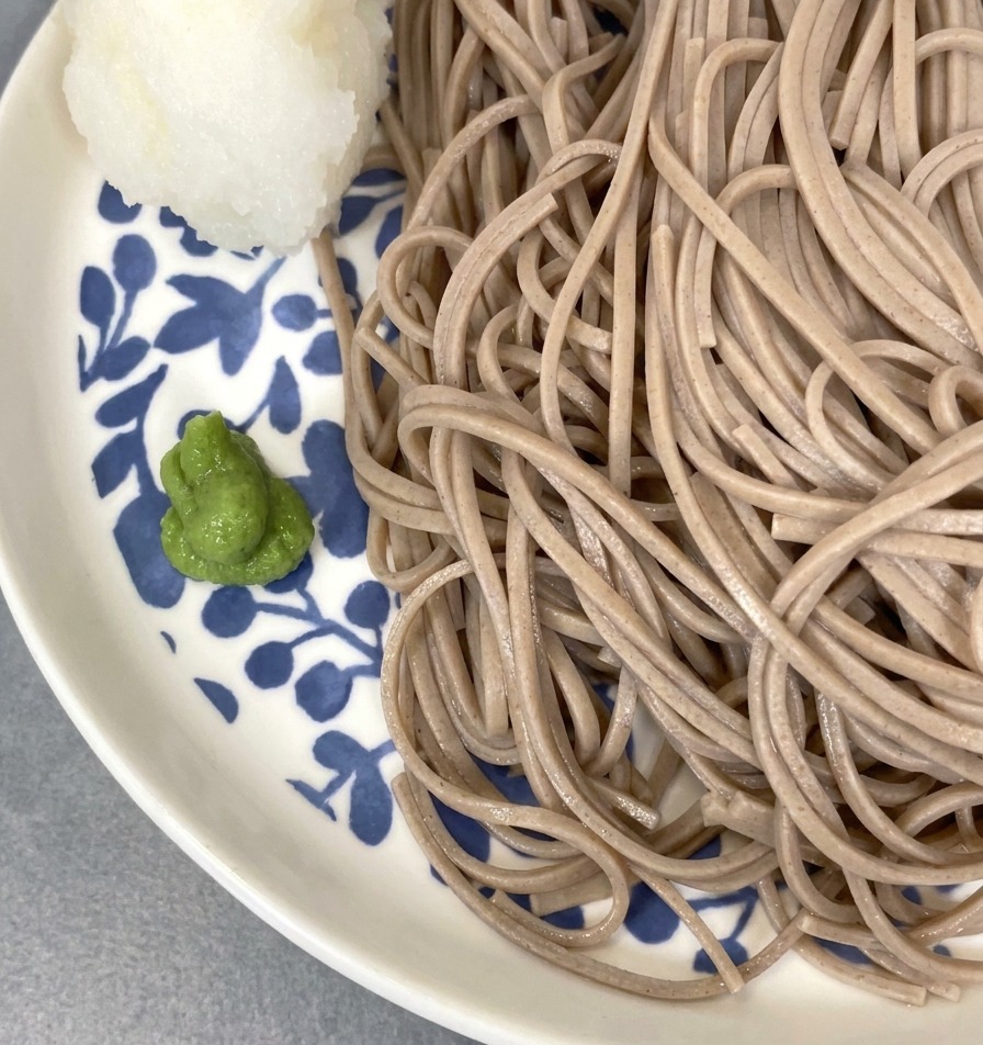 Nouilles soba servies avec une petite boule de radis râpé et une noisette de wasabi sur le bord de lassiette.