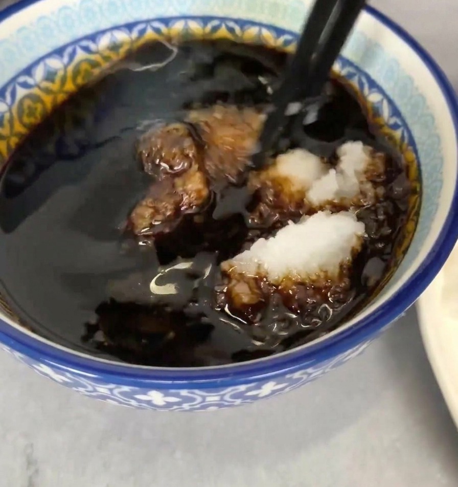 Bol de sauce sombre avec du radis râpé incorporé à laide de baguettes noires.