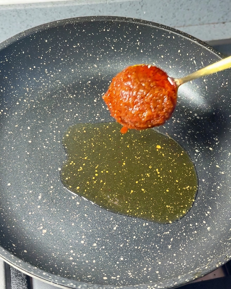 Une cuillerée de pâte de crevettes rouge épaisse ajoutée dans la poêle contenant lhuile de sésame.