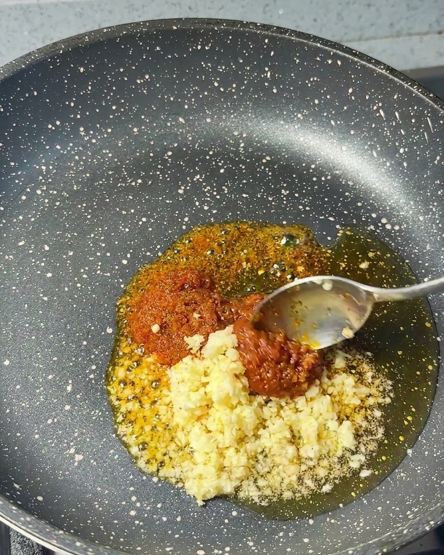 Ail haché ajouté à la cuillère dans une poêle contenant déjà la pâte de crevettes et lhuile.