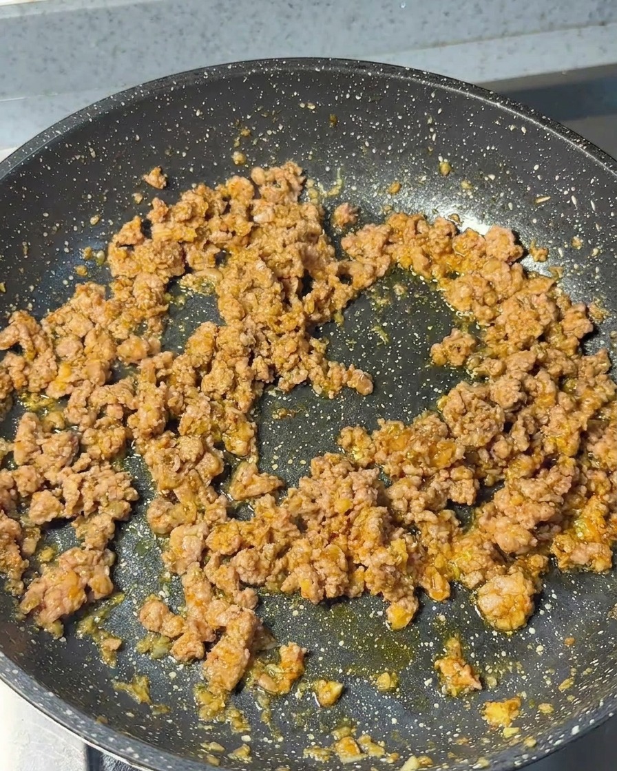 Porc haché cuisant dans la poêle avec les aromates, présentant une texture dorée et granuleuse.