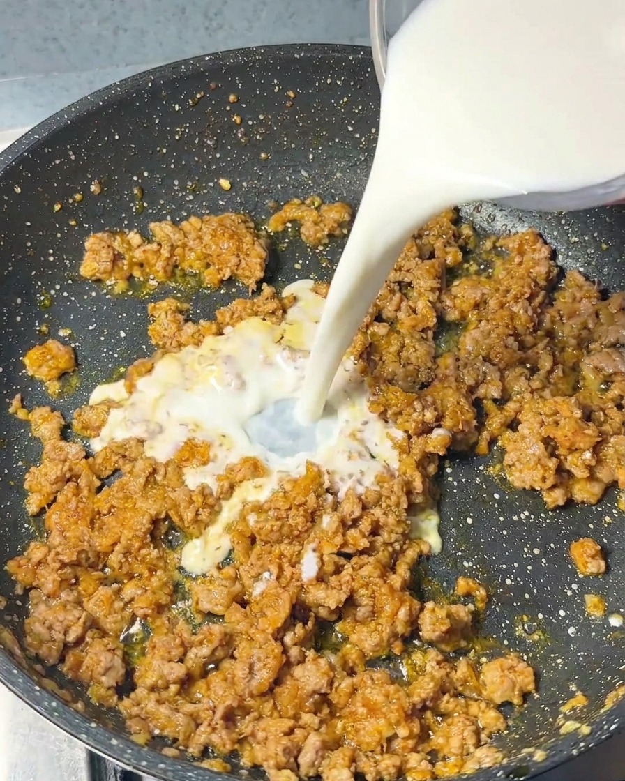 Filet de lait blanc versé dun récipient en verre dans la poêle contenant le porc cuit et les assaisonnements.
