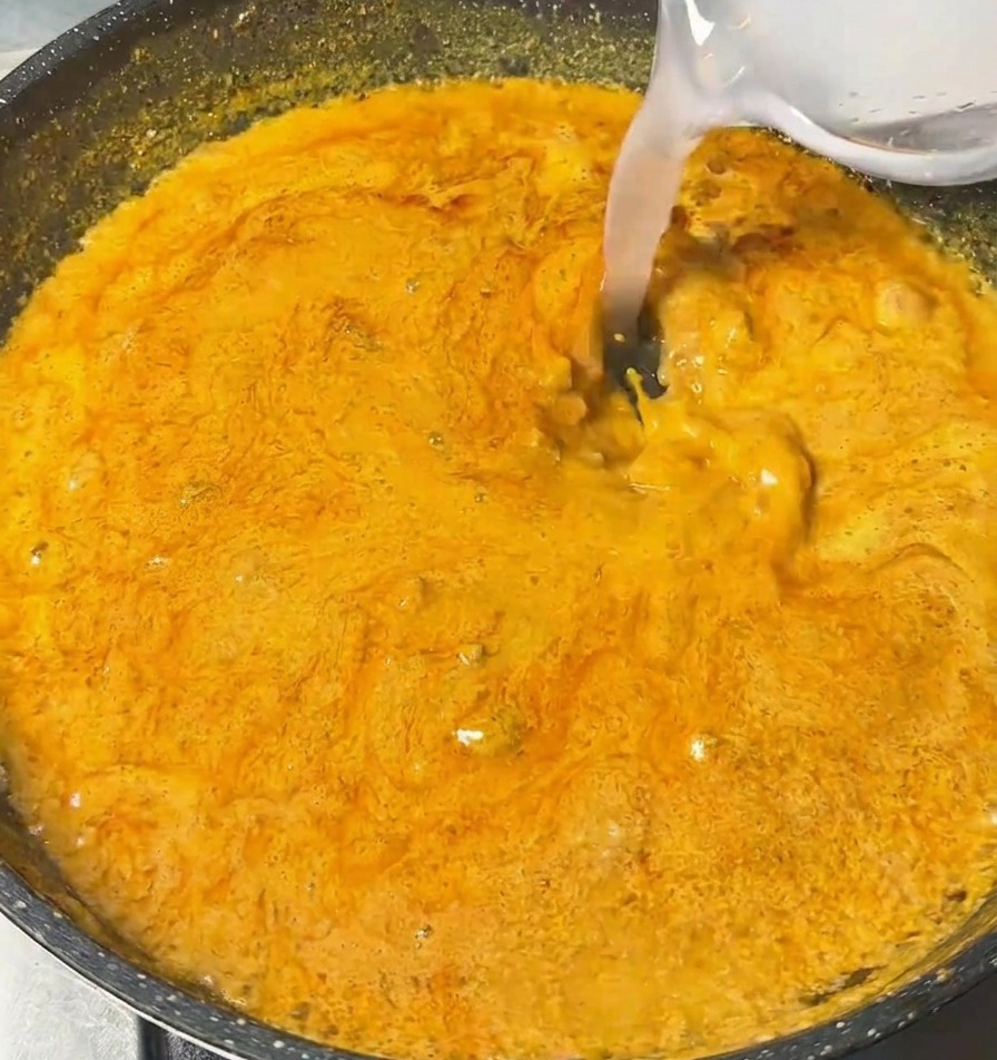 Liquide clair versé dun petit bol dans une poêle de sauce curry orange épaisse et frémissante.