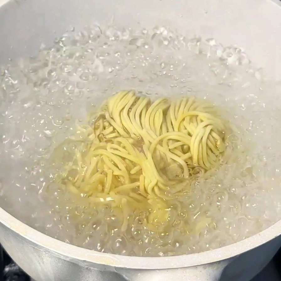 Un nid de nouilles ramen japonaises cuisant dans une casserole deau en pleine ébullition.