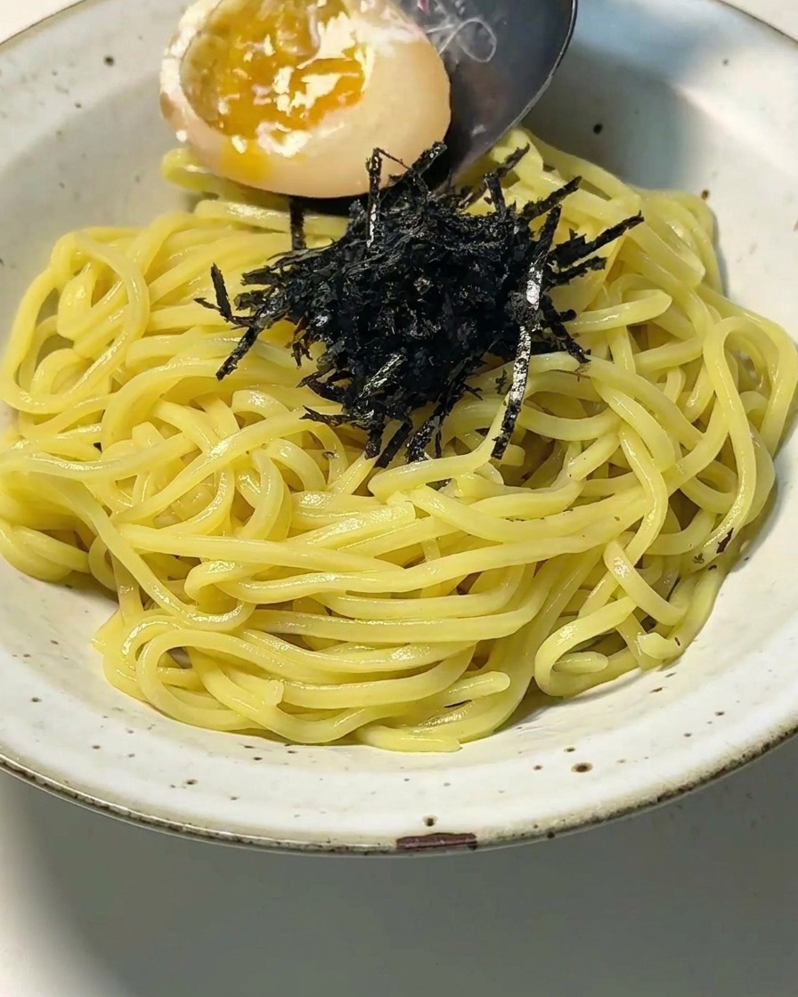 Gros plan dun bol de nouilles et de nori alors quune cuillère dépose un œuf mollet coupé en deux au jaune brillant.
