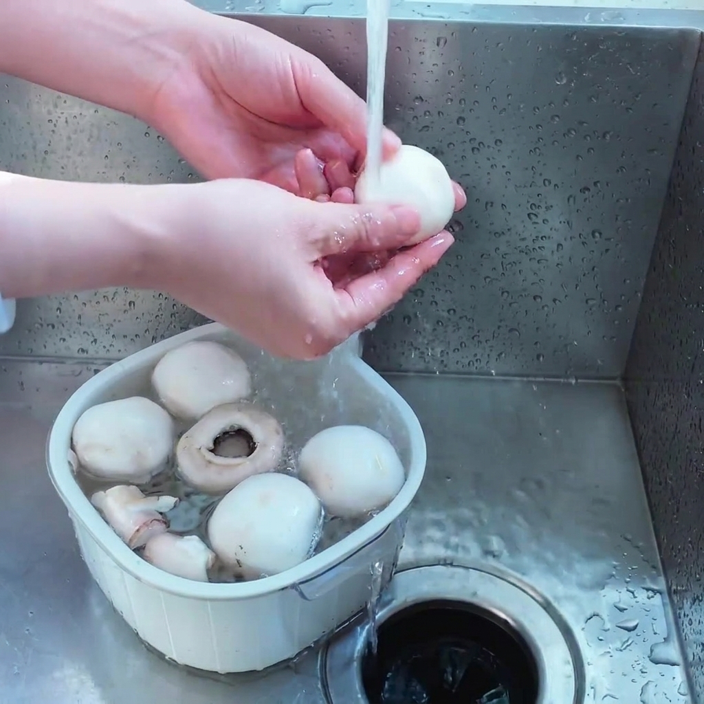 Une personne lavant des champignons de Paris entiers dans une passoire blanche sous leau du robinet.
