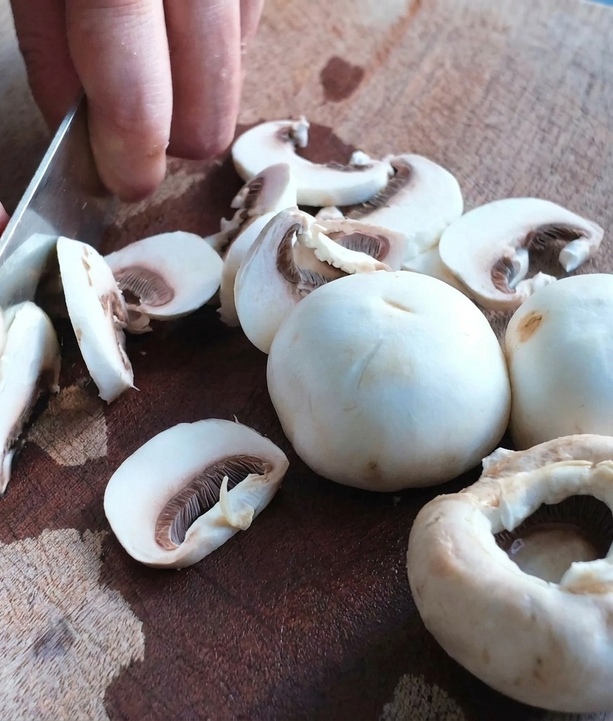 Gros plan dun couteau de chef coupant des champignons de Paris sur une planche en bois.