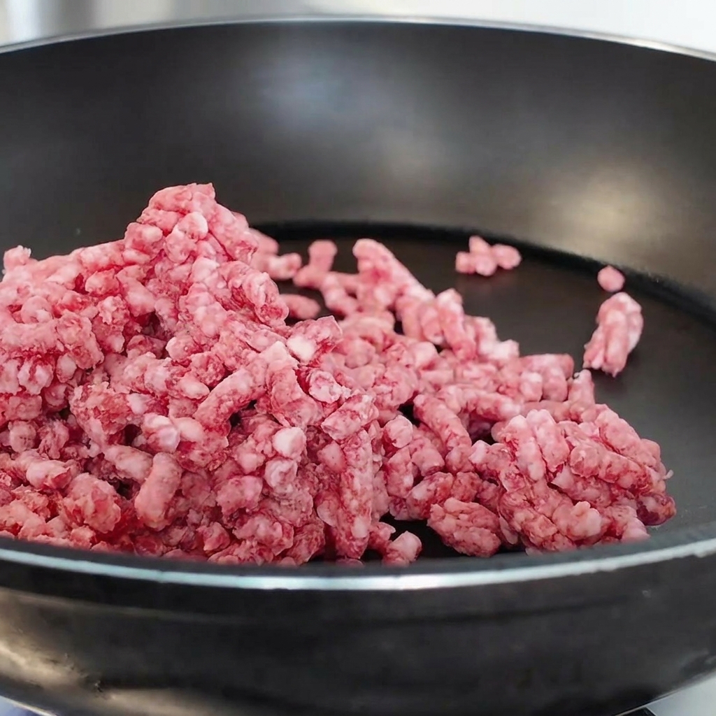 Bœuf haché cru en train dêtre émietté et cuit dans une poêle antiadhésive noire.