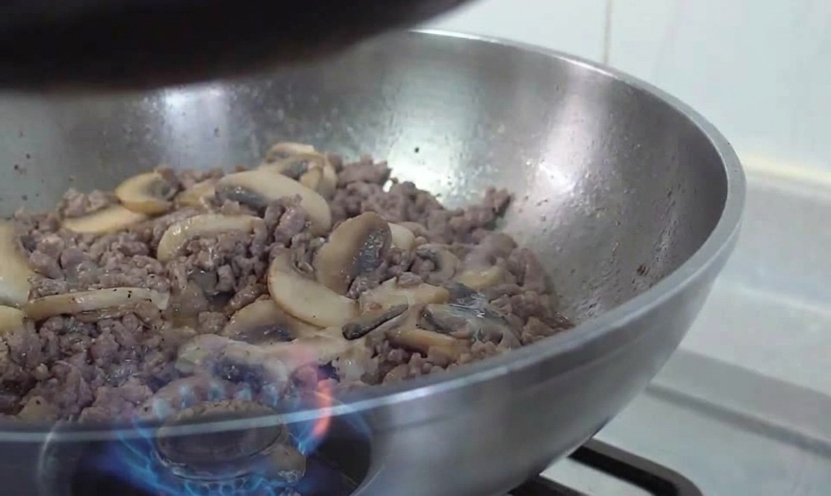 Préparation de bœuf et champignons sautés dans une poêle au-dessus dune flamme de gaz.