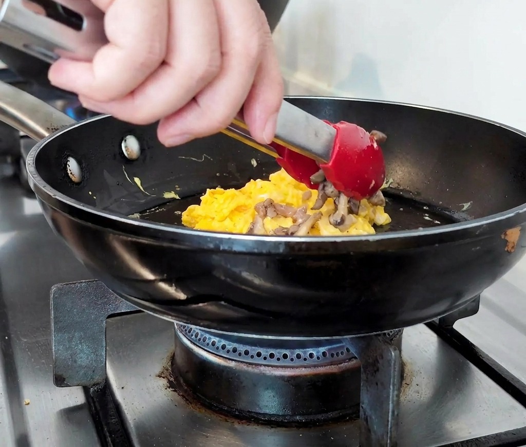 Bœuf haché et champignons cuits déposés sur le lit dœufs moelleux dans la poêle.