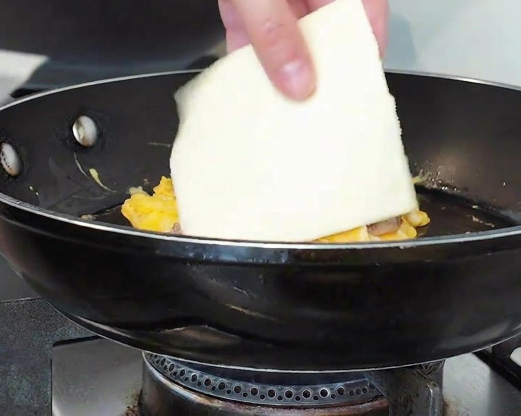 Une main posant une tranche carrée de fromage sur le dôme de viande et dœufs.
