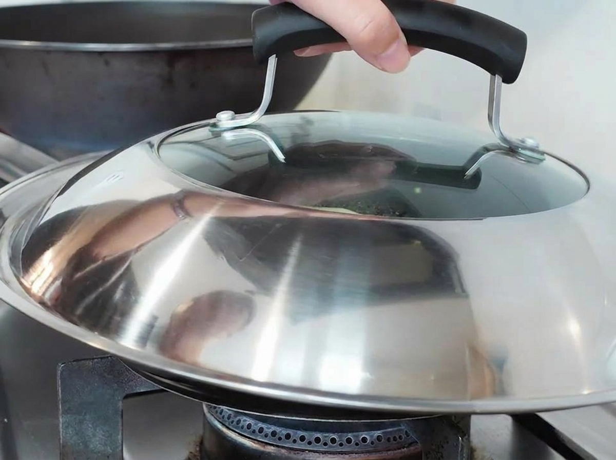 Une main posant un grand couvercle sur une poêle de cuisson sur une gazinière.