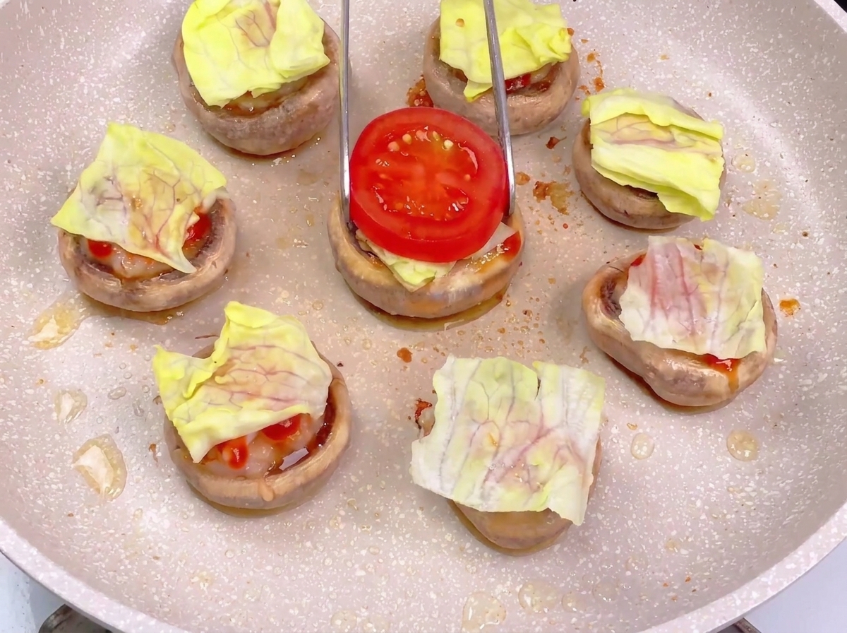 Utilisation dune pince pour placer une tranche de tomate rouge sur une base de burger de champignon déjà garnie de laitue et de sauce.