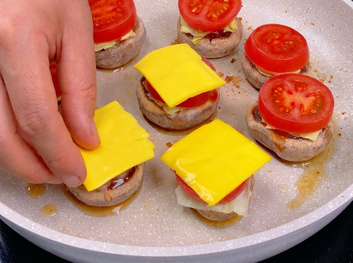 Une main déposant un carré de fromage jaune sur une tranche de tomate lors de lassemblage dun burger de champignon.