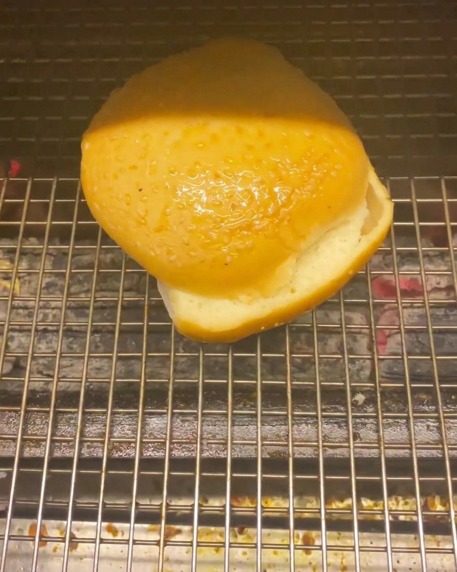 Un pain à burger posé sur une grille au-dessus de braises chaudes pour le faire griller.