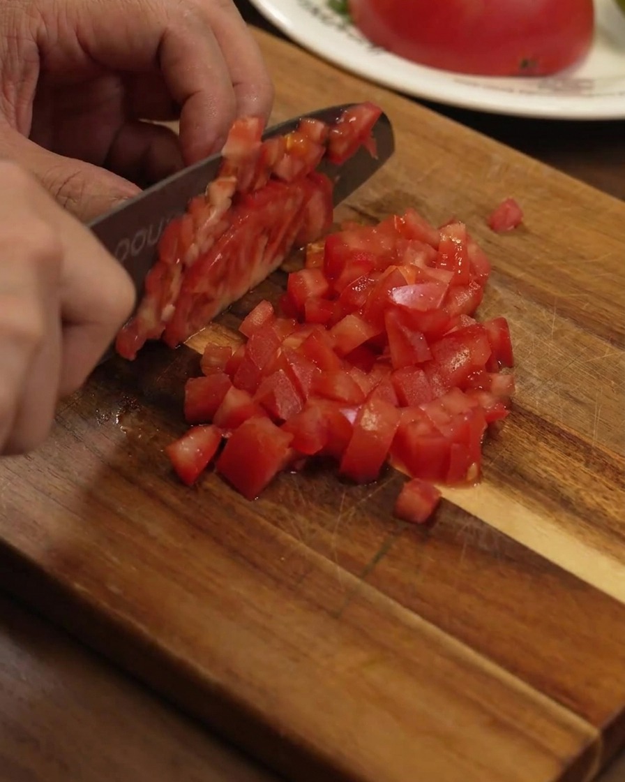 Dés de tomates rouges mûres coupés uniformément sur une planche en bois avec un couteau de chef.