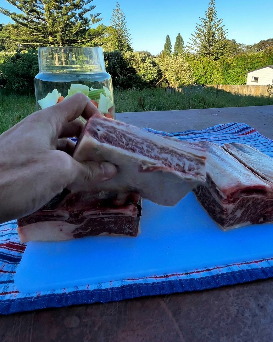 Une main tenant une épaisse côte de bœuf crue au-dessus dun bocal en verre rempli de légumes hachés.