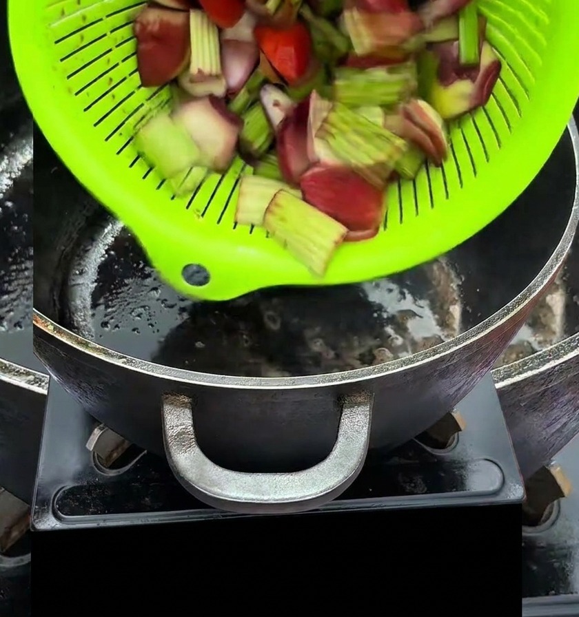 Des légumes hachés versés depuis une passoire verte dans une cocotte noire chaude.