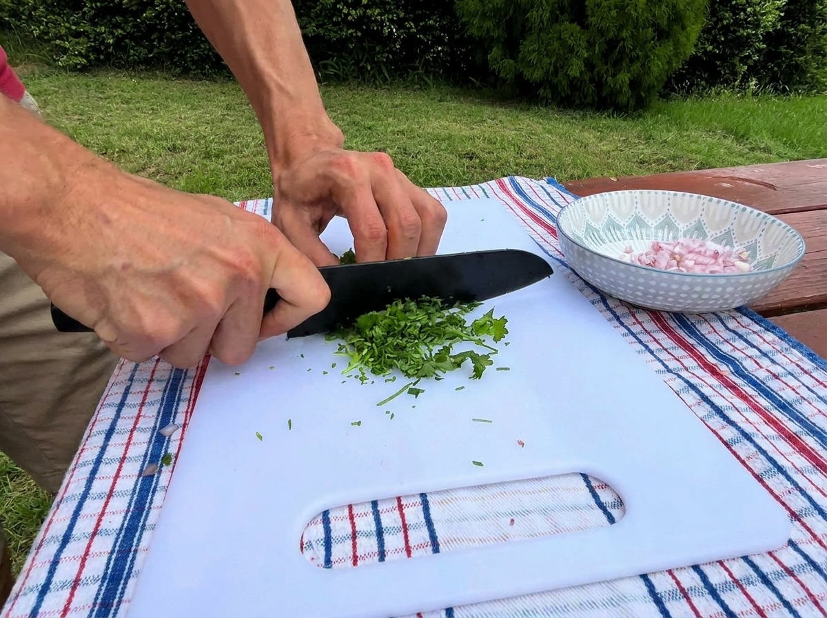 Une personne utilisant un couteau de chef pour hacher finement du persil vert sur une planche blanche, à côté dun bol déchalotes.
