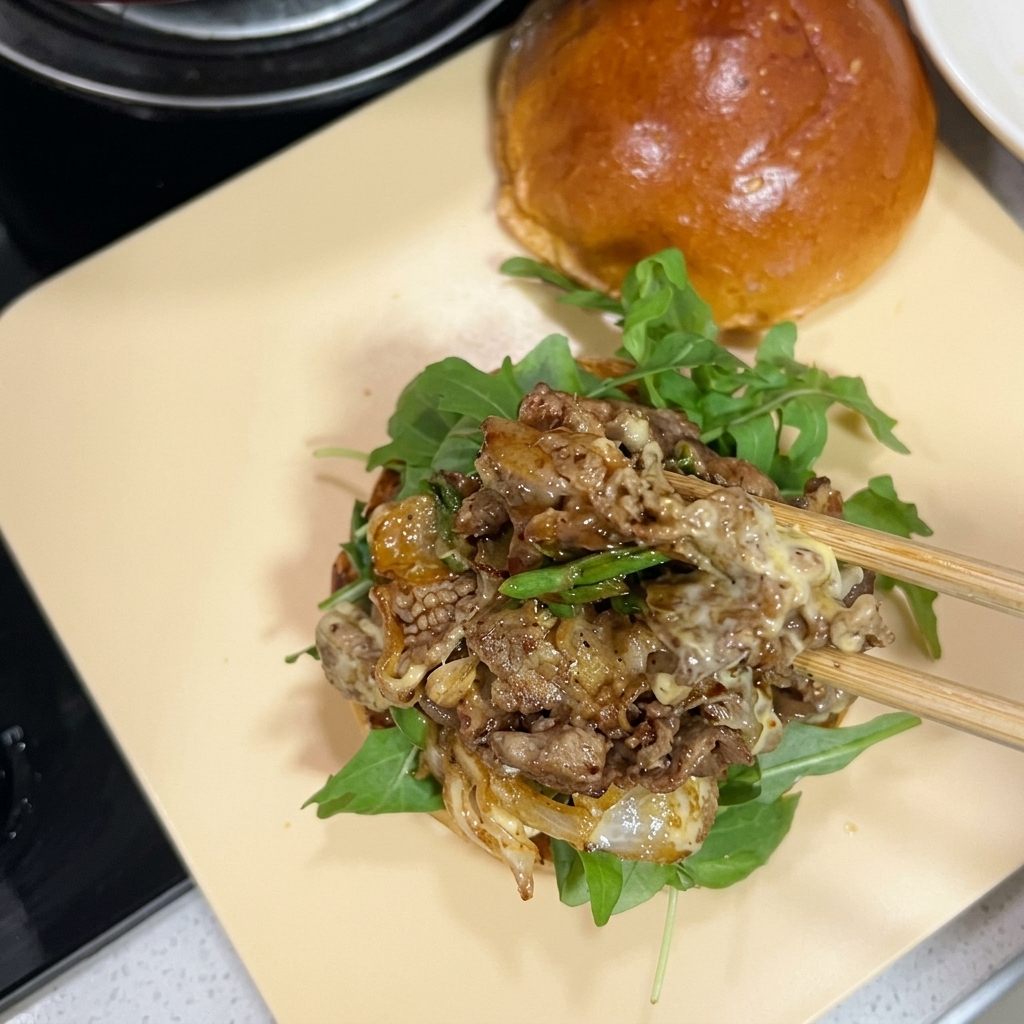 Des baguettes transférant une portion généreuse de bœuf sauté au fromage fondu sur un pain à burger garni de roquette.