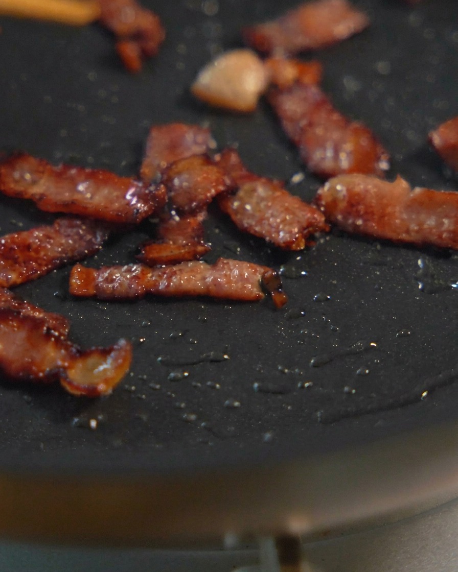 Petits dés de bacon grésillant dans une poêle noire, montrant différentes étapes de coloration dorée.