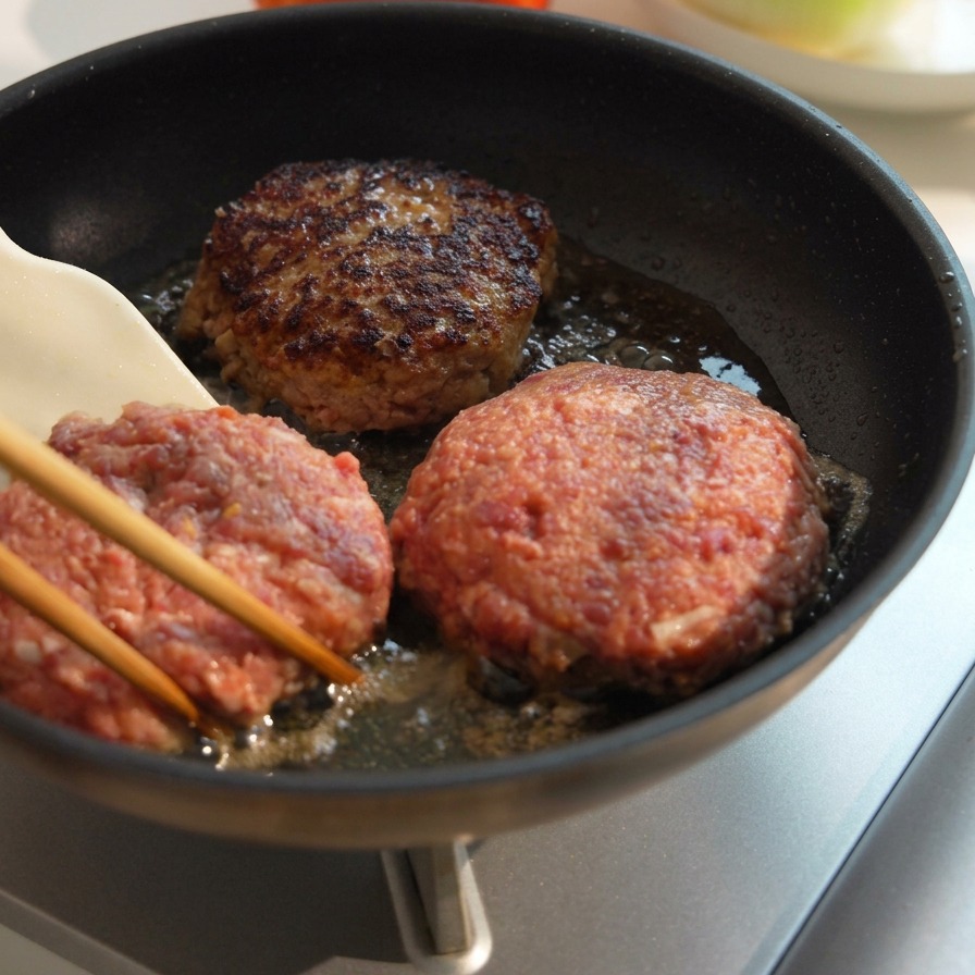 Trois steaks de bœuf épais cuisant dans une poêle, lun deux retourné montrant une croûte bien brune et caramélisée.