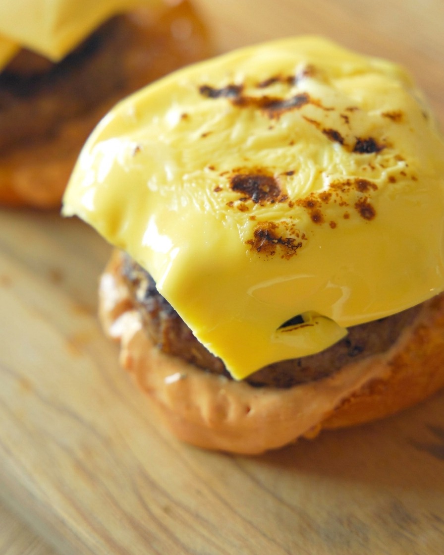 Gros plan dune tranche de cheddar fondu et légèrement brûlé sur un steak de bœuf posé sur son pain.