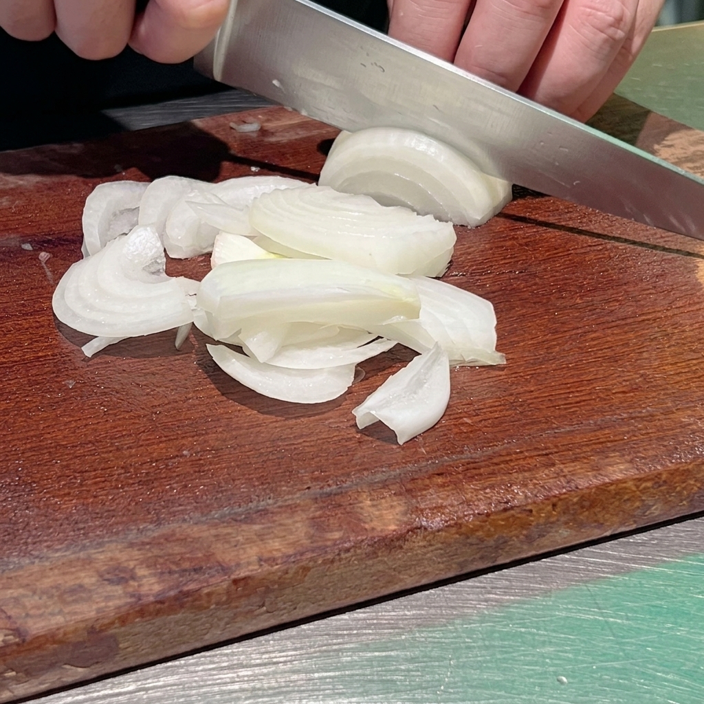 Gros plan dun chef utilisant un couteau de cuisine tranchant pour émincer un oignon blanc en fines lanières sur une planche en bois sombre.