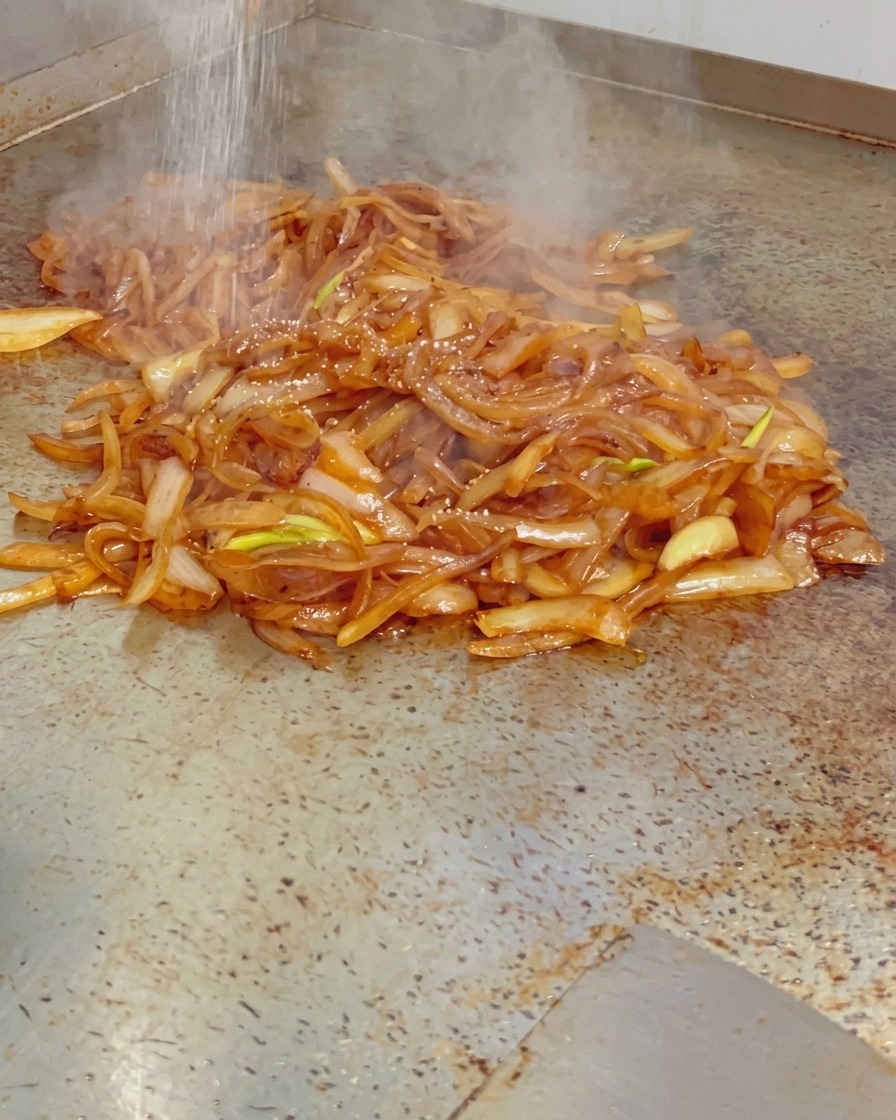 Du sel fin saupoudré sur des oignons caramélisés brillants et fumants sur une plaque de cuisson chaude.