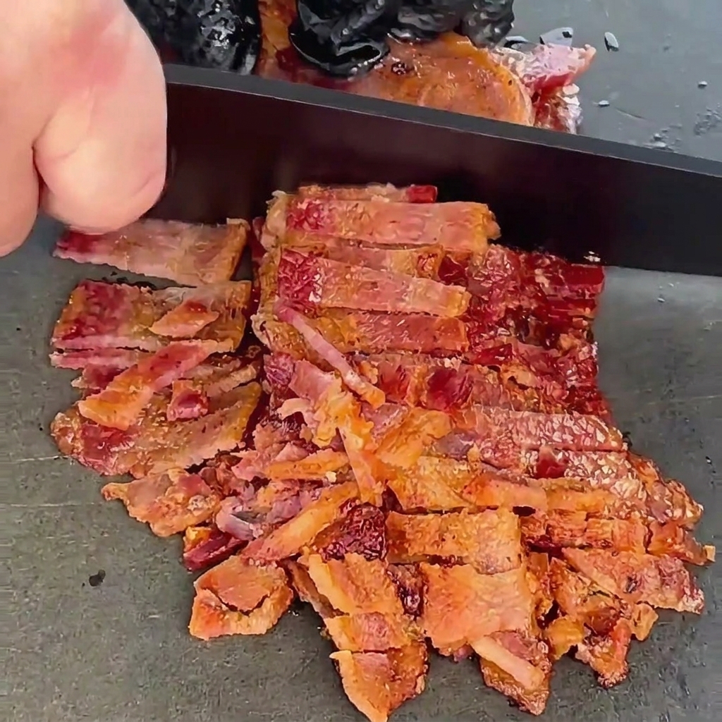 Tranches de bacon croustillantes cuites en train dêtre finement hachées avec un couteau de chef sur une planche sombre.