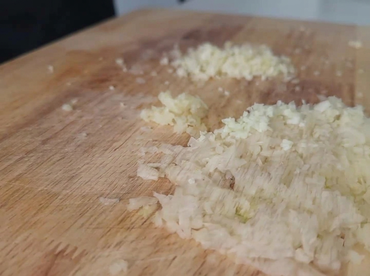 De loignon blanc et de lail finement émincés et répartis sur une planche à découper en bois clair.