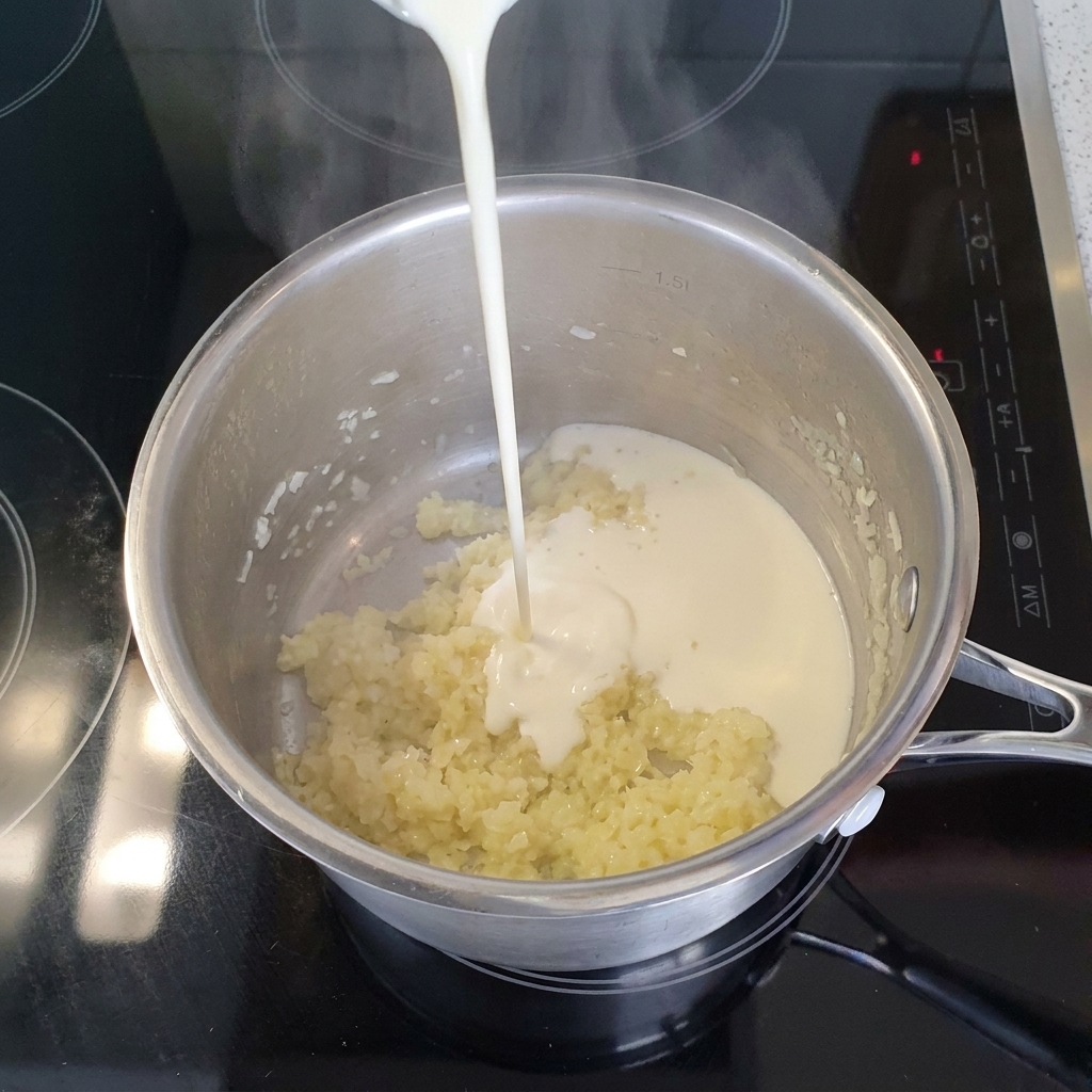 Un filet de crème légère liquide versé dans une casserole en inox contenant les oignons et lail cuits.
