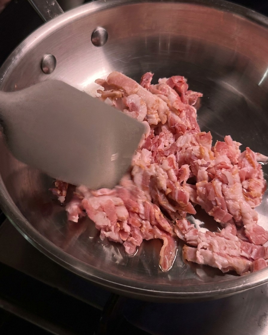 Morceaux de bacon cru coupés en dés remués et cuits avec une spatule métallique dans une poêle en acier inoxydable chaude.