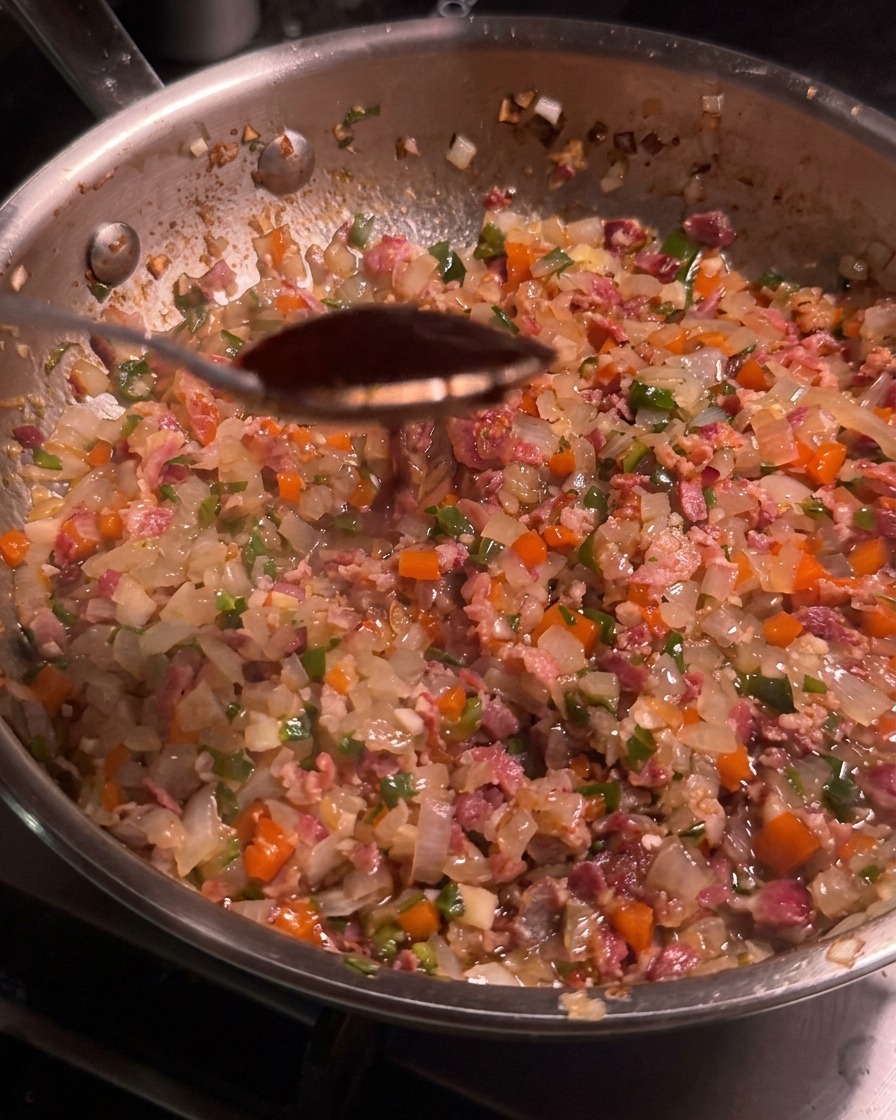 Une cuillérée de sauce chipotle foncée au-dessus dune poêle remplie dun mélange de bacon et de légumes.
