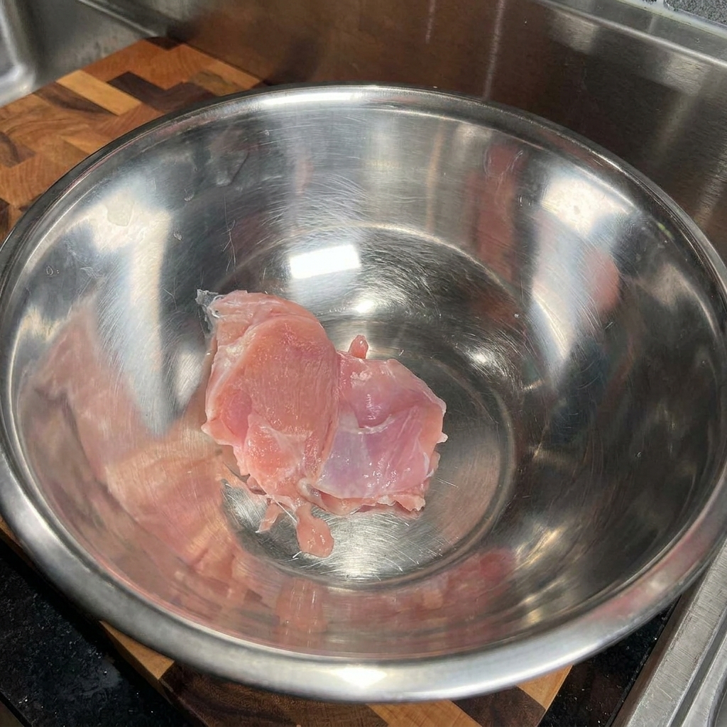 Hauts de cuisse de poulet crus placés dans un grand cul-de-poule en acier inoxydable vide.