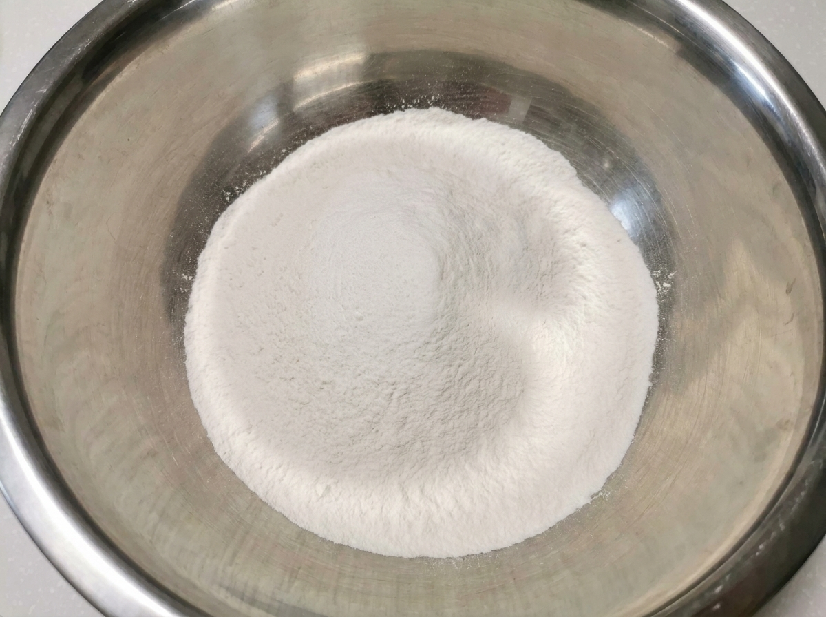 Un dôme blanc de farine de riz et de farine tout usage mélangées dans un grand cul-de-poule propre en acier inoxydable.