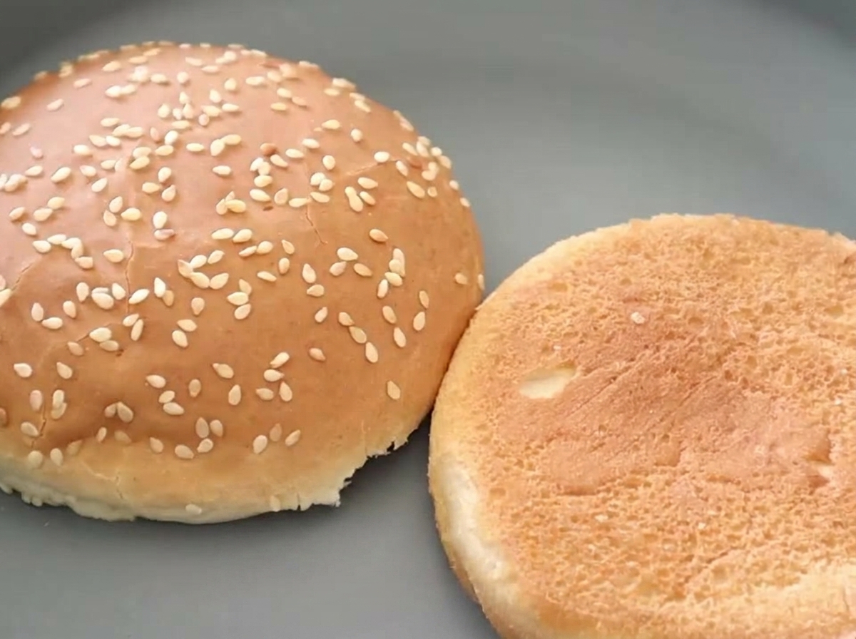 Deux moitiés de pain à burger aux graines de sésame côte à côte, dont lune présente un intérieur magnifiquement doré.