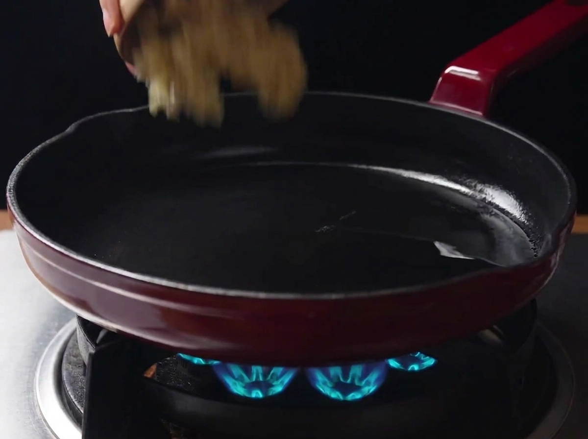 Ail haché versé depuis un petit bol dans une poêle chaude contenant de lhuile de cuisson sur une cuisinière à gaz allumée.