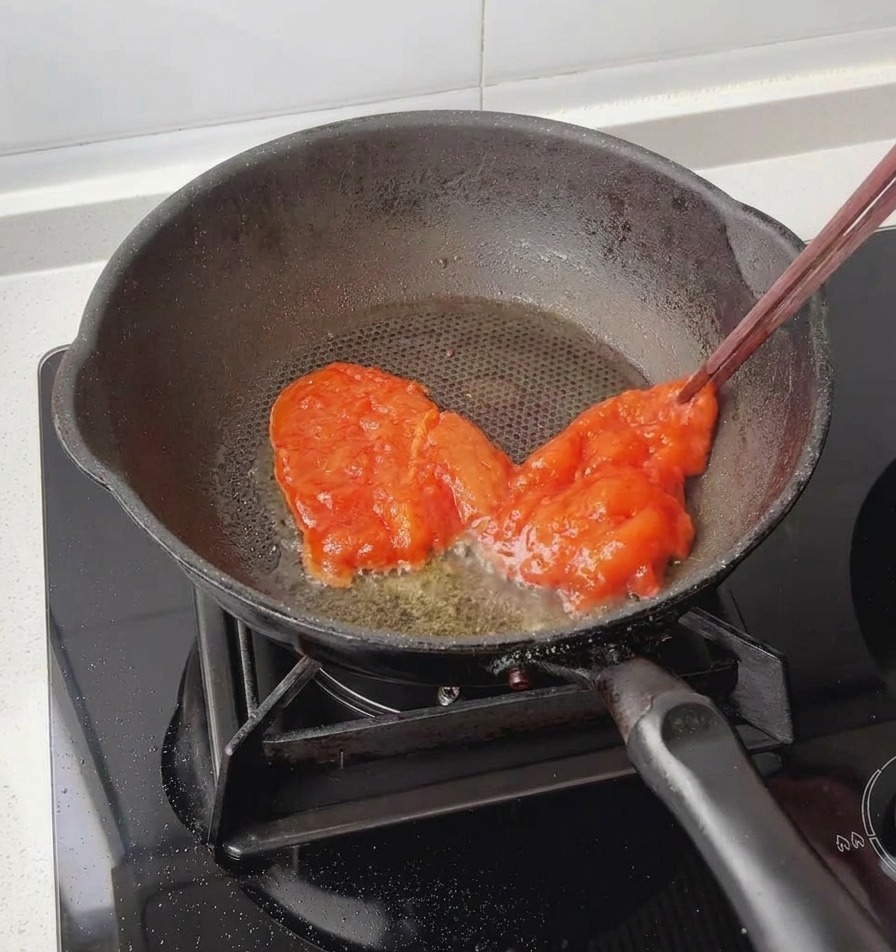Des baguettes utilisées pour déposer un blanc de poulet rouge, bien mariné, dans une poêle noire légèrement huilée.