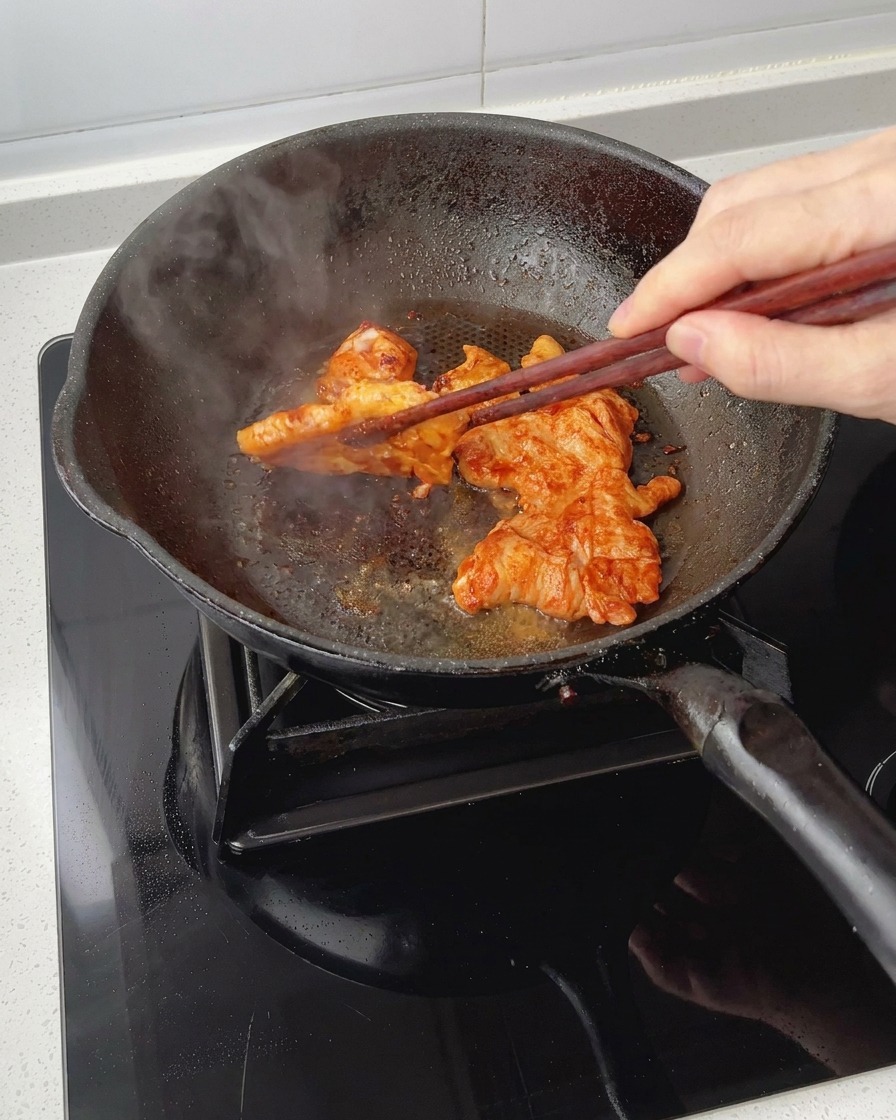 Cuisson de morceaux de blanc de poulet mariné dans une poêle, retournés à laide de baguettes, affichant une surface laquée et caramélisée.