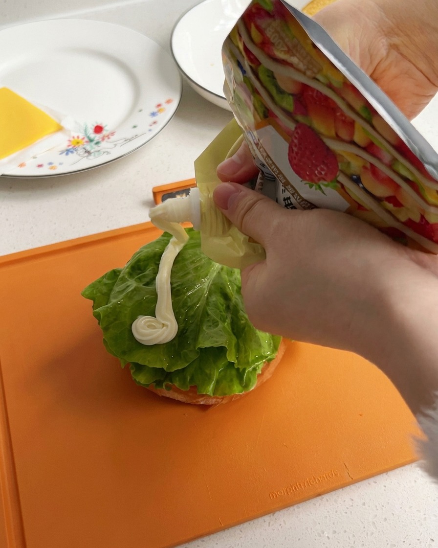 De la mayonnaise blanche et crémeuse versée en un cordon épais sur une feuille de laitue verte posée sur la base dun pain à burger.