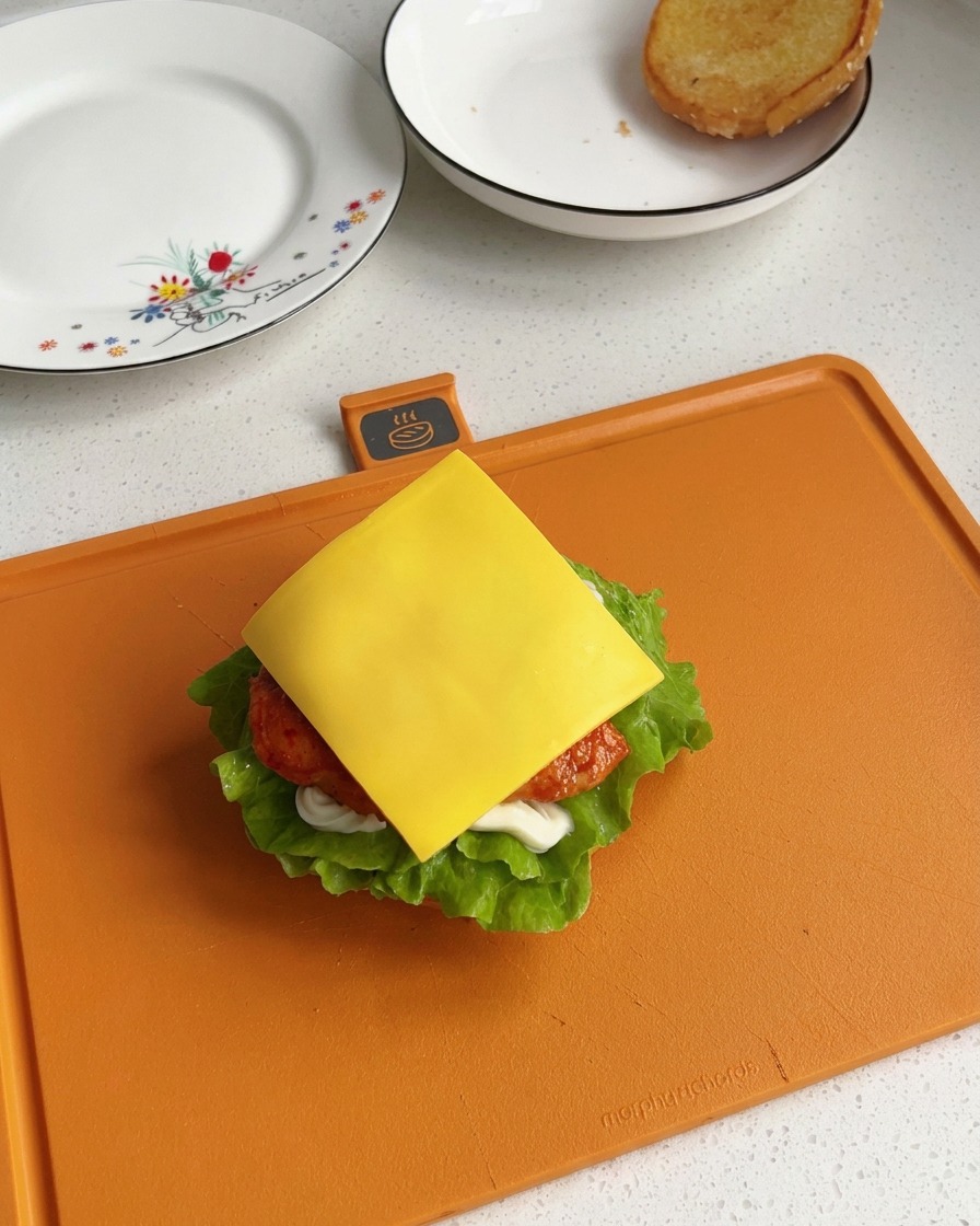 Une tranche carrée de fromage fondu jaune vif posée bien à plat sur un morceau de poulet chaud au cœur dun burger en cours de montage.