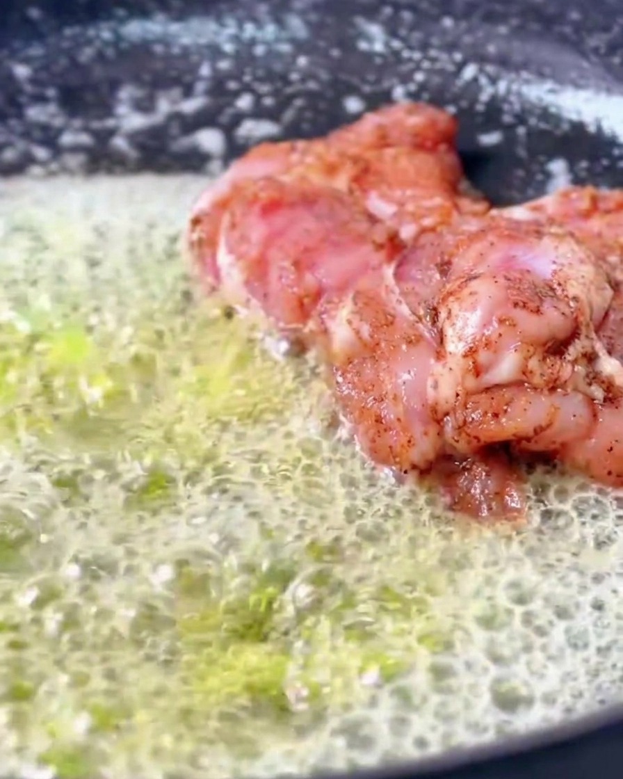 Des hauts de cuisse de poulet cajun marinés cuisant dans une poêle remplie dune généreuse quantité de beurre fondu qui bulle et mousse.