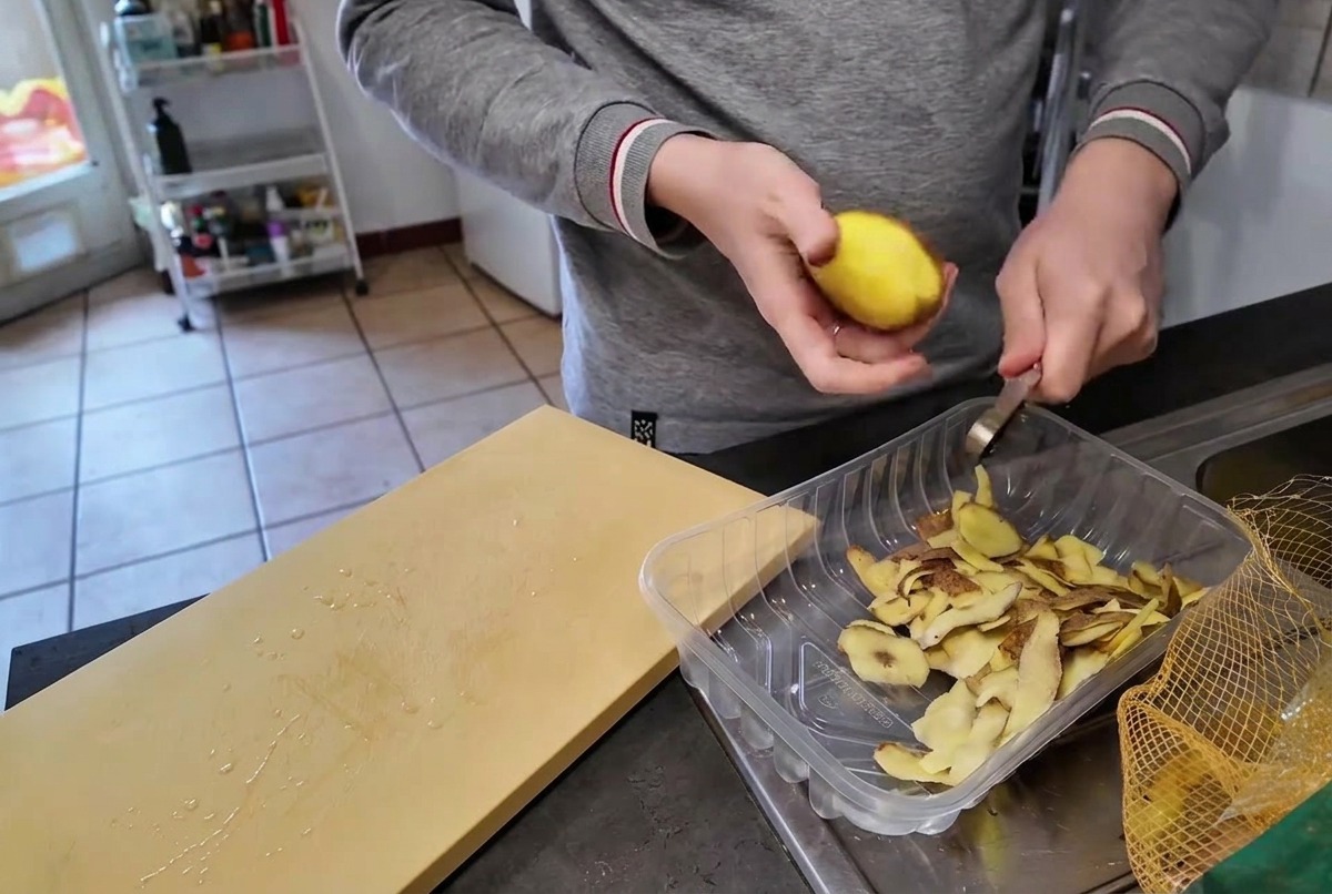 Une personne épluchant une pomme de terre jaune crue avec un petit couteau au-dessus dun bac en plastique transparent.